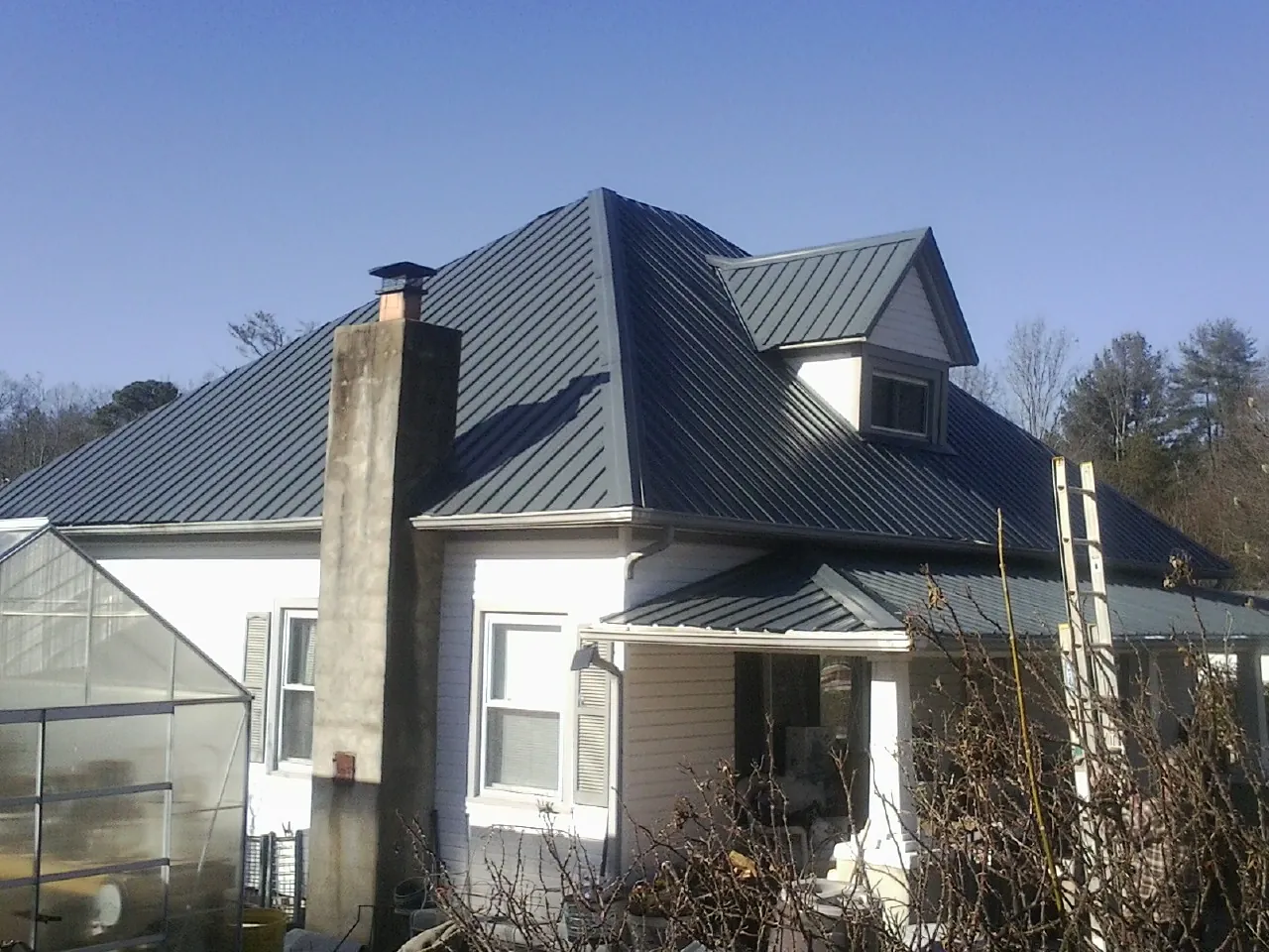 Dark blue standing seam metal roof on a white farmhouse with dormer — Slate & Tile Roof Repair by Roofing Brothers in Paupack