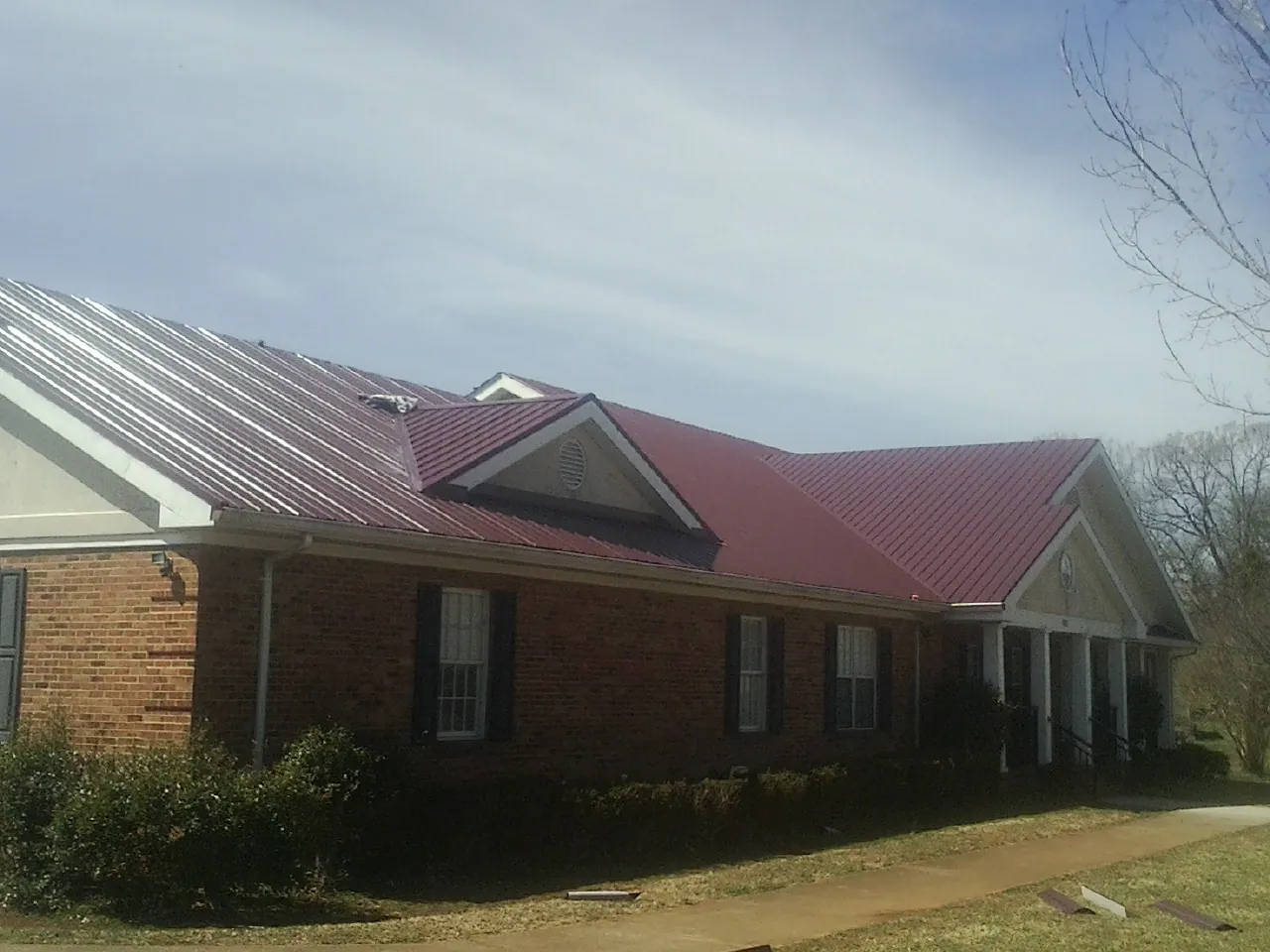 Red metal roof with gabled entries on a long brick building, from a Hail Damage Roof Repair job in Paupack