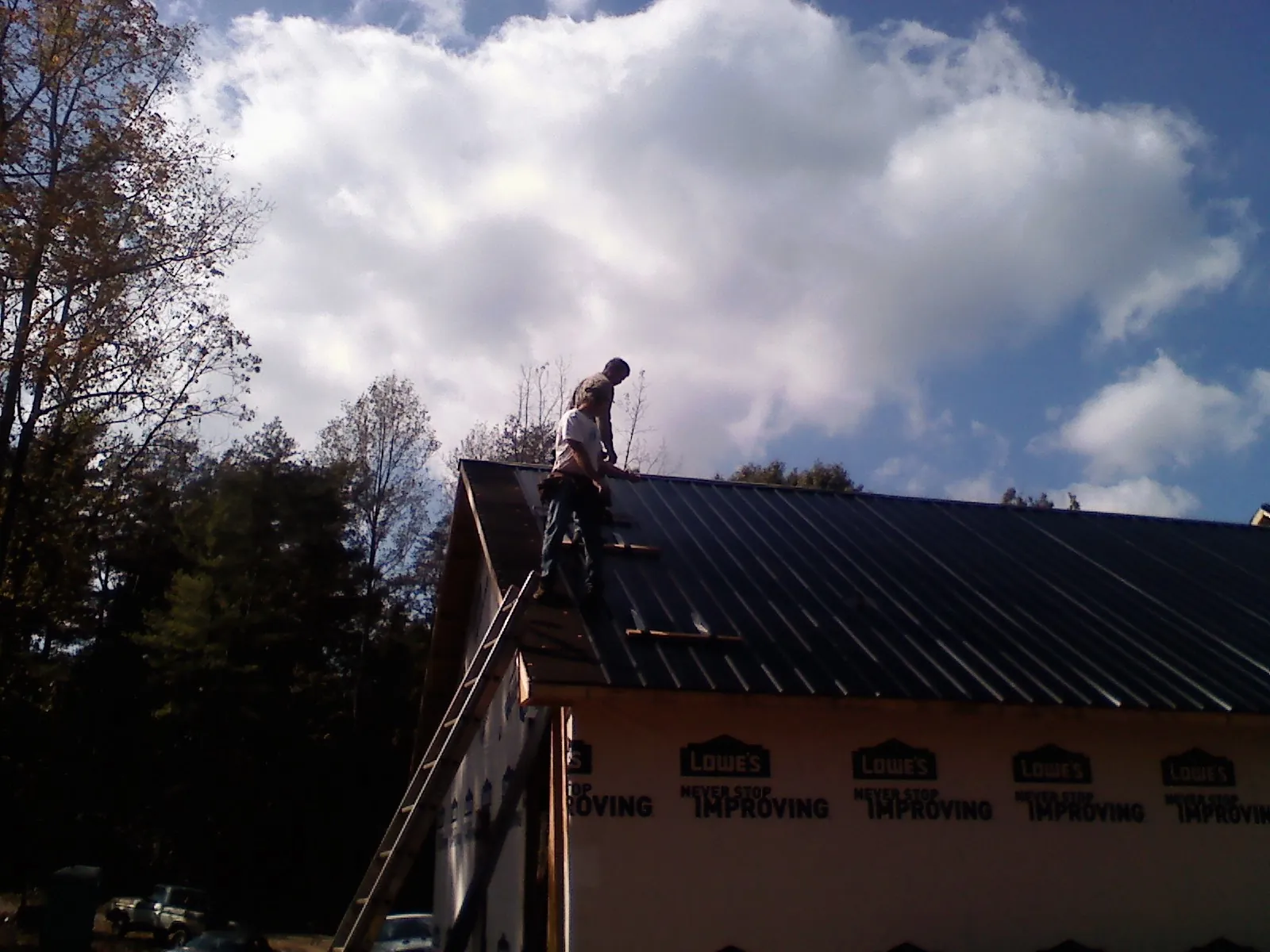 Roofer fastening dark metal panels high against a cloudy sky, from a Roof Inspection job in Paupack
